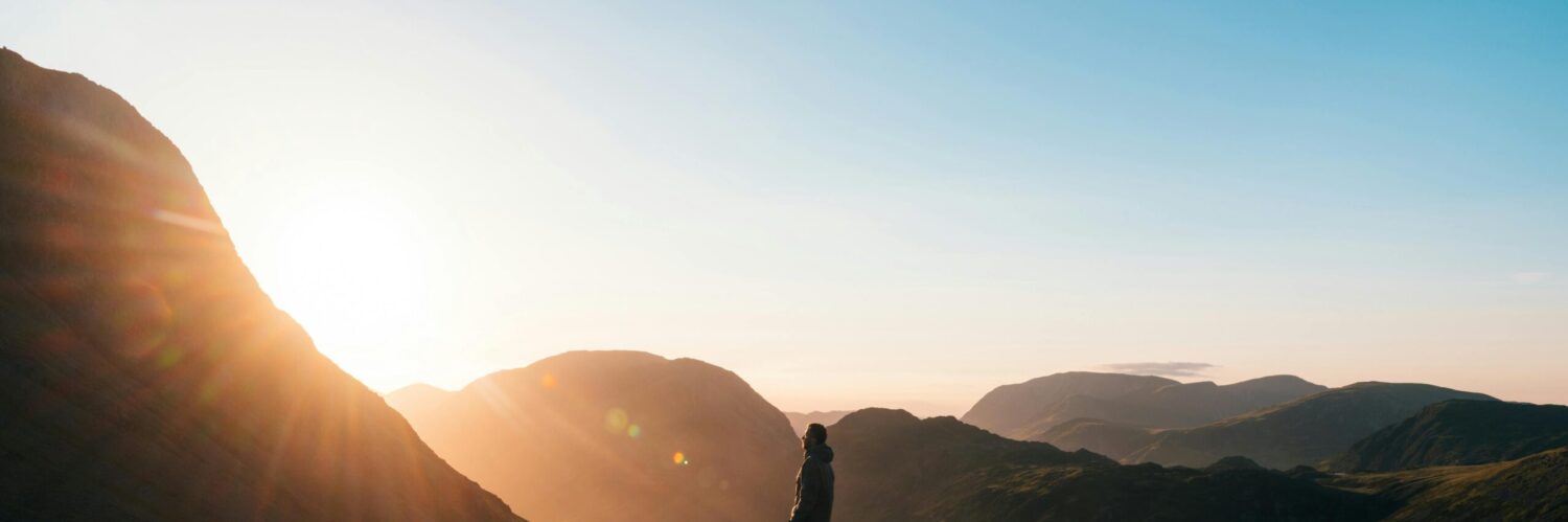 Silhouette of a person standing on a hill during sunrise in Cumbria, England with scenic mountain views.